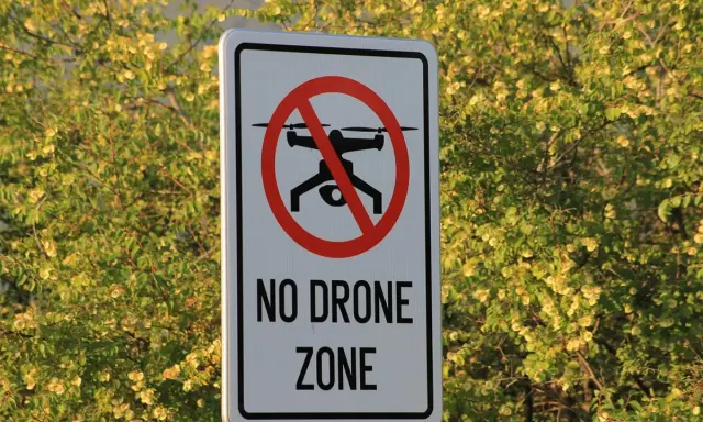 Cartello "No Drone Zone" in Italia, con un drone barrato. La natura circostante è rigogliosa e verde.
