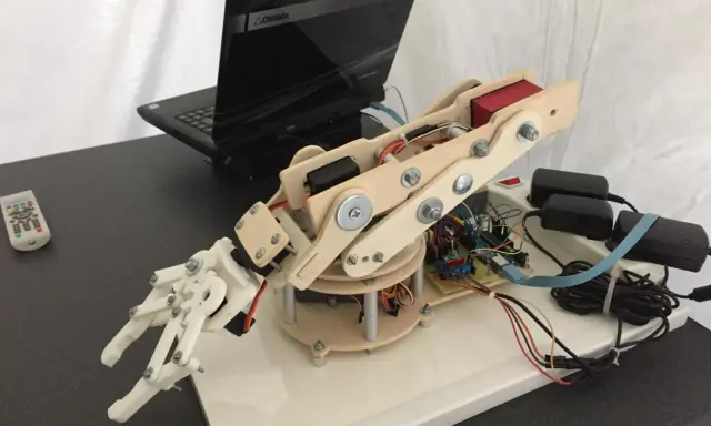 Mano robotica Arduino in legno e plastica, collegata a un laptop e alimentata da adattatori.