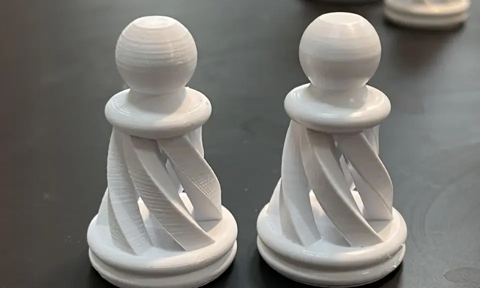 Due pedine degli scacchi bianche, stampate in 3D con filamento pla acetone, con un design a spirale.