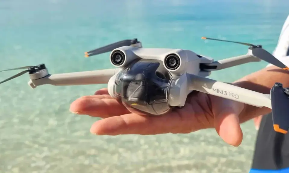 Un drone Mini 3 Pro tenuto in mano su una spiaggia tropicale, pronto per foto droni mozzafiato.