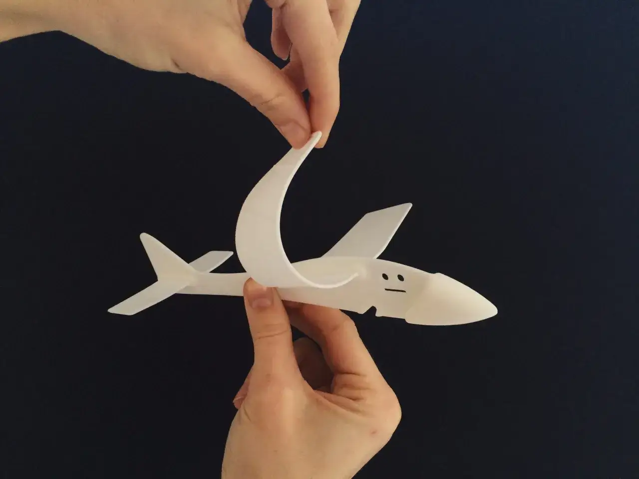 Mani tengono uno squalo bianco stampato in 3D con nylon, con un'espressione facciale disegnata.
