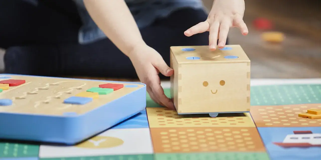 Bambino interagisce con un dado sorridente e blocchi colorati, esplorando i giochi di programmazione su un tappeto interattivo.