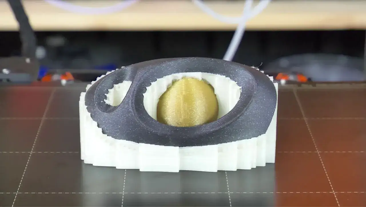 Stampa 3D di un oggetto con un nucleo dorato, circondato da strati bianchi e una cornice esterna grigia. Il materiale PVA viene utilizzato per i supporti.