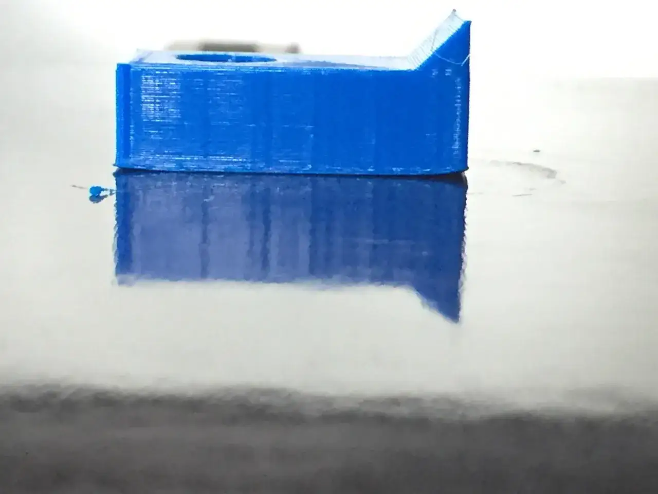 Oggetto blu stampato in 3D con un leggero warping, riflesso su superficie lucida.