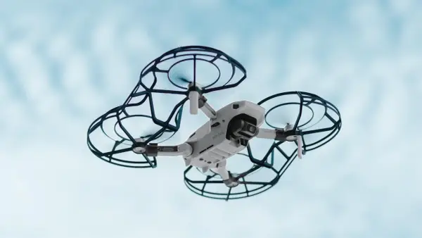 Un drone bianco con protezioni nere vola nel cielo azzurro. Perfetto per la tua scuola di droni.