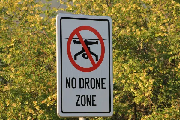 Cartello "No Drone Zone" in Italia, con un drone barrato. La natura circostante è rigogliosa e verde.
